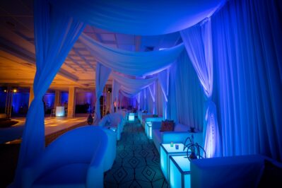 A lounge area with white sofas and glowing blue cube tables, draped with white curtains under soft blue lighting, creates an elegant ambiance—perfect for entertainment services Suffolk and Nassau County, NY.