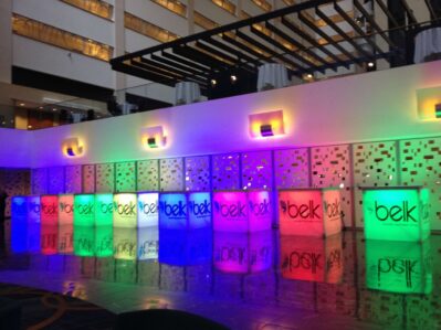 Colorful illuminated bar counters with "belk" displayed on each, reflecting on a shiny floor in a modern indoor space—perfect for entertainment services Suffolk and Nassau County, NY, or upscale events seeking a vibrant atmosphere.