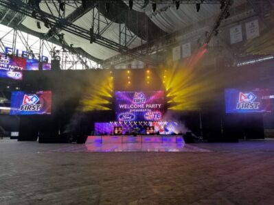 Large indoor stage with colorful lights and smoke effects, featuring a big screen that reads "FIRST Welcome Party presented by Ford." Two side screens show the FIRST logo—perfect for top-tier entertainment services in Suffolk and Nassau County, NY.