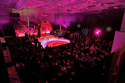 A large indoor NY event with pink and purple lighting, a crowded dance floor with colorful lights, illuminated star-shaped decorations, and people socializing around tables in a festive atmosphere—perfect for DJ services Suffolk and Nassau County, NY.