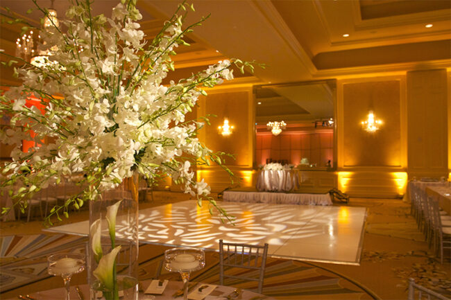 A lavish ballroom in NY,NY decorated for an event, featuring a large bouquet of white flowers in the foreground and a lit, patterned dance floor—perfect for unforgettable nights with DJ services in Suffolk and Nassau County.