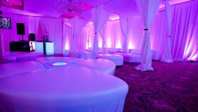A lounge area with white cushioned seating, draped white curtains, and purple-pink ambient lighting creates an elegant, modern atmosphere—perfect for events or parties featuring entertainment services in Suffolk and Nassau County, NY.