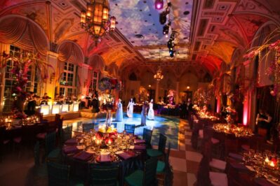 A lavish NY ballroom decorated with elegant lighting, colorful flowers, and round dining tables set for guests. People dance on a large, illuminated floor under ornate ceilings—perfect for dj services Suffolk and Nassau County.