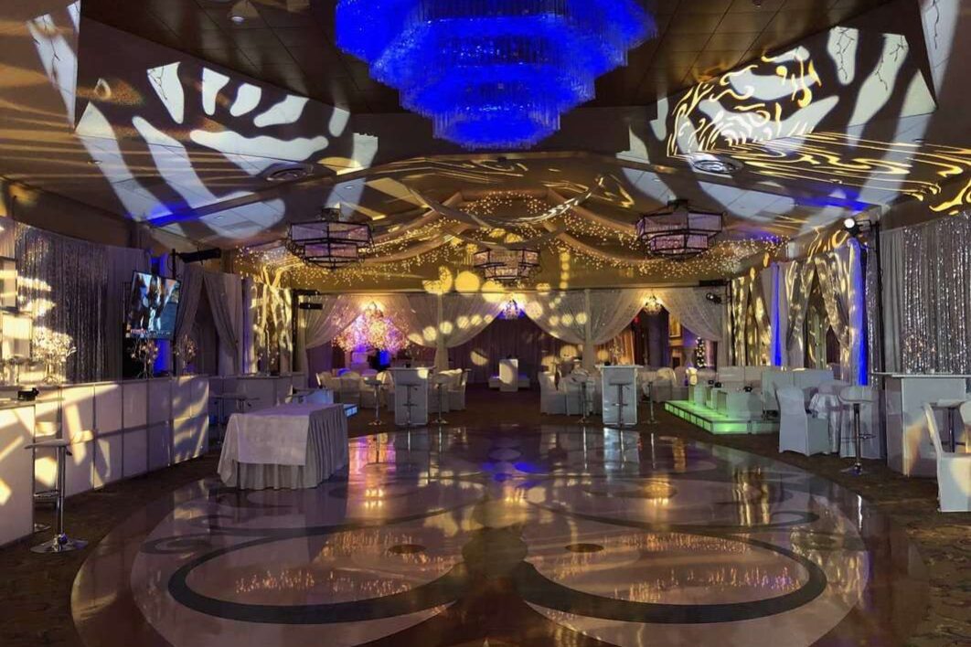 A lavish event hall in NY, decorated with shimmering lights, draped white fabric, and patterned spotlight projections. Enhance your celebration with top entertainment services Suffolk and Nassau County as guests mingle among elegant tables and lounge seating.