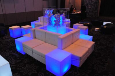 A modern lounge setup in NY features white cube seats and glowing blue illuminated cubes arranged around a central sculpture, perfect for events seeking dj services Suffolk and Nassau County, NY, creating a futuristic ambiance in a dimly lit room.
