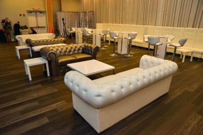 Modern lounge in NY,NY with tufted white and brown leather sofas, white chairs, and tables on a dark wood floor. White drapes frame the space, where guests mingle—perfect for events needing DJ services in Suffolk and Nassau County.
