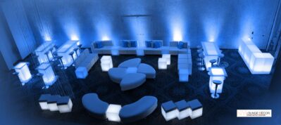 A modern lounge setup with white illuminated furniture, including sofas, tables, and stools, arranged in a spacious room with blue accent lighting and a patterned dark floor—ideal for entertainment services in Suffolk and Nassau County, NY.