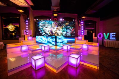A vibrant stage setup in NY features illuminated white steps, glowing cube seats, colorful abstract face art on a digital screen, and large "LOVE" letters lit up—perfect for entertainment services Suffolk and Nassau County.