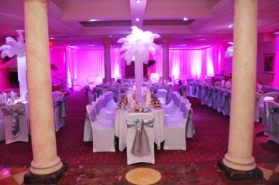 Elegant banquet hall with purple lighting, white linens, silver chair bows, and tall feather centerpieces for a festive, glamorous atmosphere—perfect for celebrations paired with professional DJ services Suffolk and Nassau County, NY.