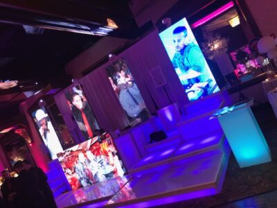 A vibrant event space in NY with large illuminated screens displaying DJs and performers, colorful lights, and a modern white stage setup—perfect for energetic parties and premier DJ services in Suffolk and Nassau County, NY.