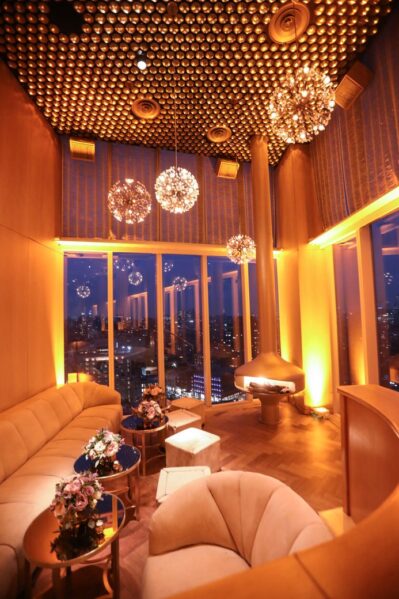 A luxurious NY lounge with plush seating, round tables, and elegant flower arrangements, featuring floor-to-ceiling windows overlooking the city skyline at dusk—perfect for entertainment services Suffolk and Nassau County.