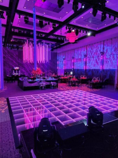 A modern event venue in NY with purple lighting, a glowing LED dance floor, elegant table settings, and projected patterns on the walls, offering vibrant entertainment services for Suffolk and Nassau County in a futuristic atmosphere.