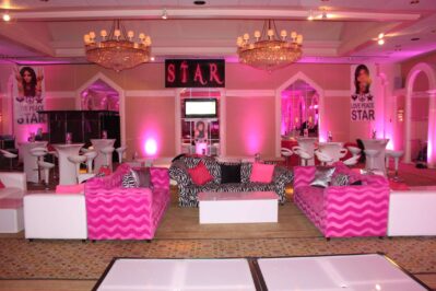 A vibrant NY lounge with pink lighting, pink zigzag and zebra-print sofas, white chairs and tables, chandeliers, and posters of a woman with the words “LOVE PEACE STAR”—offering standout entertainment services Suffolk and Nassau County, NY.