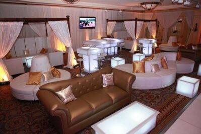 A modern lounge area with gold and white sofas, glowing tables, and sheer curtains creates a stylish atmosphere—perfect for entertainment services Suffolk and Nassau County, NY.