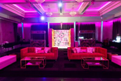 A lounge area with red sofas, glass tables, and heart-shaped pillows is set in a room with purple lighting. Perfect for entertainment services Suffolk and Nassau County, NY, it features drink and patch bars and a graffiti-style mural between them.