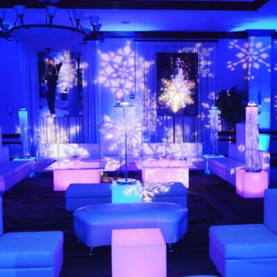 A lounge area with white furniture and glowing pink and blue cube tables, illuminated by blue lighting and snowflake-shaped light projections—perfect for entertainment services in Suffolk and Nassau County, NY.