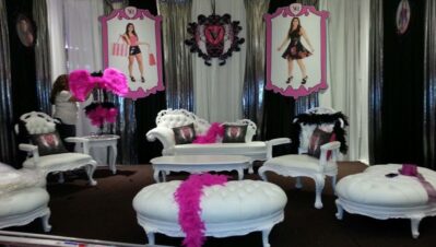 A glamorous lounge area with white vintage furniture, pink feather boas, and framed photos of a young woman in stylish outfits on the wall, set against shimmery curtains—perfect for DJ services Suffolk and Nassau County, NY.