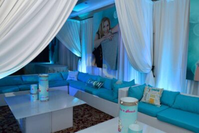 A lounge area with white drapes, modern sofas with turquoise cushions, beach-themed decor, and blue lighting creates a relaxing vibe. Perfect for entertainment services Suffolk and Nassau County, NY. A smiling girl’s photo adds a cheerful touch.