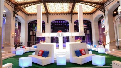 Elegant indoor lounge with white sofas, glowing cube tables, and football-themed decor. The stained glass ceiling and ornate details create a chic vibe. Ideal for entertainment services in Suffolk and Nassau County, NY, with purple ambient lighting.