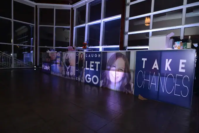 A display of large illuminated panels in a modern room, featuring photos of people and the words “LAUGH,” “LET GO,” and “TAKE CHANCES” in bold letters across the panels.